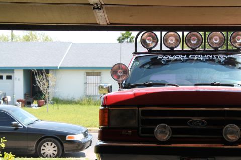 1990 Ford Bronco - Front view of a red 1990 Ford Bronco with a light bar, parked next to a black sedan.