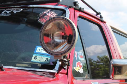 1990 Ford Bronco - Auxiliary light mounted on the A-pillar of a red vehicle, with various stickers on the windshield.