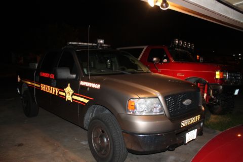 1990 Ford Bronco - A sheriff's pickup truck is parked next to a red SUV, both appearing to be in a garage or driveway at night.