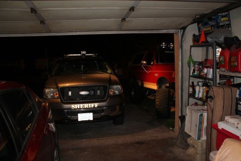 1990 Ford Bronco - Two vehicles, a Sheriff SUV and a red pickup truck, are parked inside a garage.