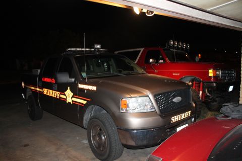 1990 Ford Bronco - Two sheriff vehicles, a pickup and a Ford Bronco, are parked side-by-side in a garage.