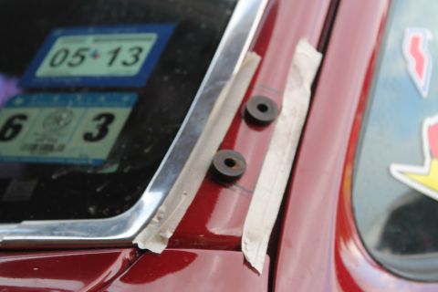 1990 Ford Bronco - Close-up of a car door showing taped-on grommets and registration stickers on the window.
