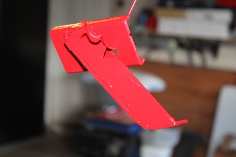 1990 Ford Bronco - A red metal bracket is shown, possibly a car part, against a blurred background.