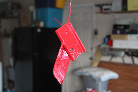 1990 Ford Bronco - A red painted metal bracket is shown hanging by a wire, likely in a garage or workshop setting.