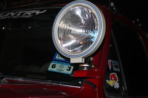 1990 Ford Bronco - A close-up of a spotlight mounted on the A-pillar of a red vehicle, with various stickers adorning the exterior.
