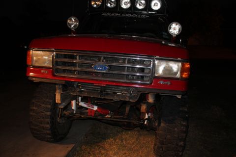 1990 Ford Bronco - Frontal view of a modified red Ford truck, equipped with multiple auxiliary lights and off-road suspension components.