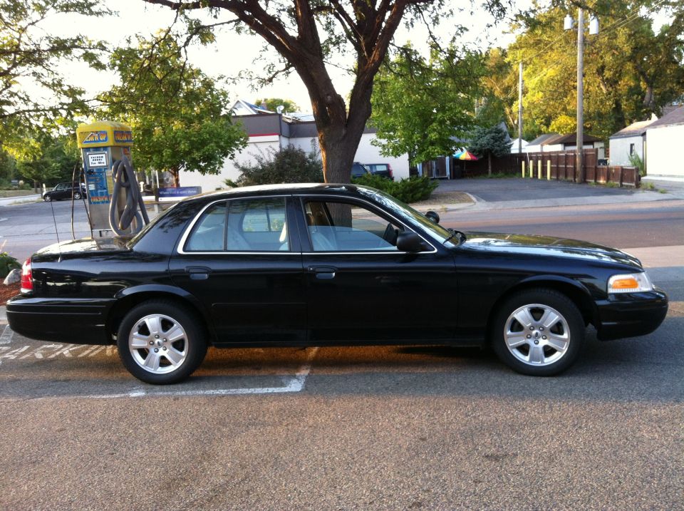 Black Ford Crown Victoria sedan, passenger side view, parked in a lot near a vacuum station