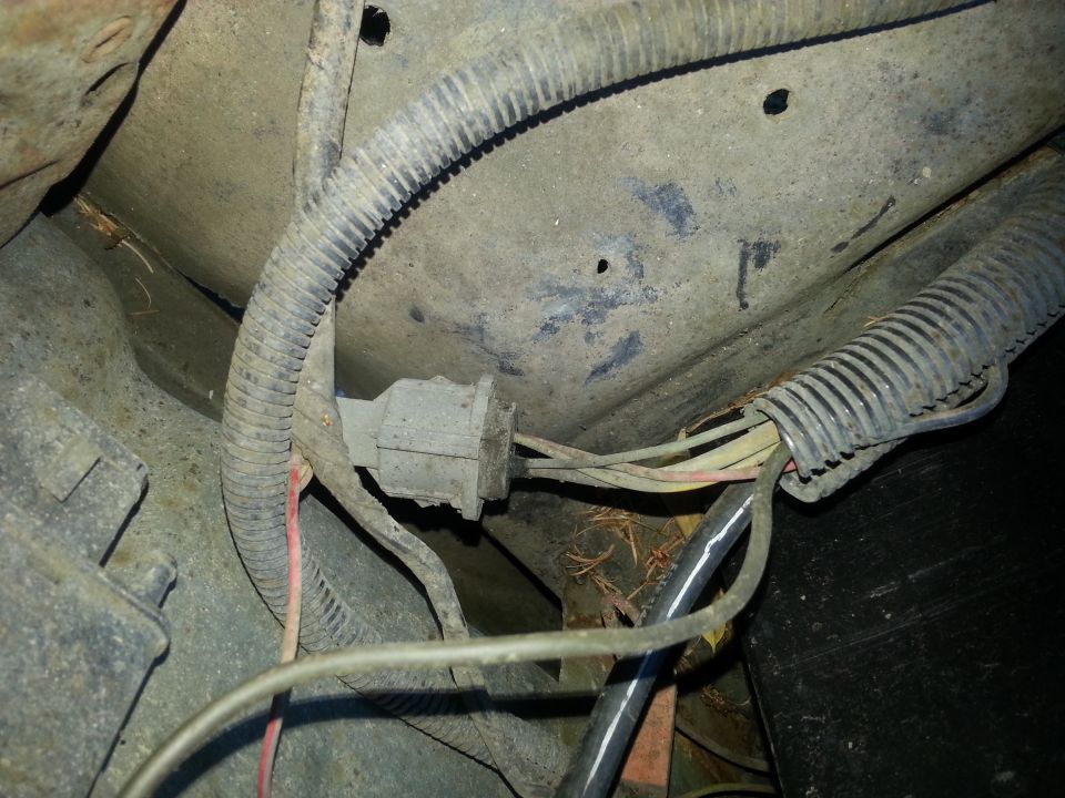 Close-up of a gray electrical connector and wiring harness attached to a dirty vehicle chassis