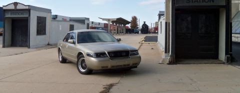 2000 Mercury Grand Marquis - A gold Mercury Grand Marquis is parked in front of a building with 'STATION' signage.