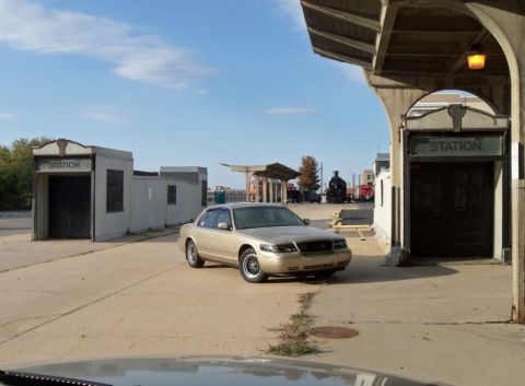 2000 Mercury Grand Marquis - A gold sedan is parked in front of a station building with a train visible in the background.