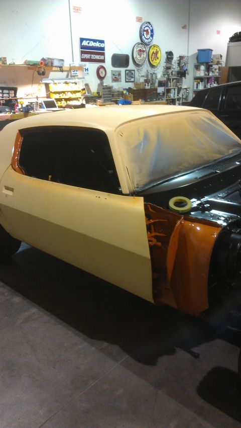 1973 Chevrolet Camaro - A classic car is undergoing restoration in a garage, with parts of it masked for painting.