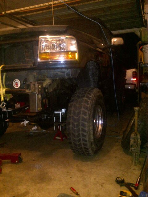 1995 Ford Bronco - The front of a Ford truck is shown in a garage, lifted on jacks with its grille removed for maintenance.