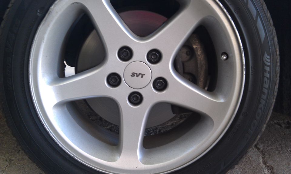 Silver 5-spoke wheel with black lug nuts and an SVT center cap