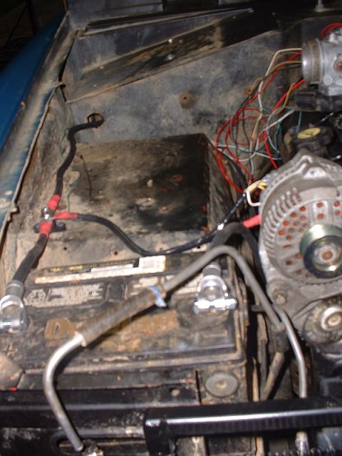 1986 Ford Bronco - The engine bay of a vehicle, a battery, alternator, and a tangle of wires, suggesting recent work or ongoing maintenance.