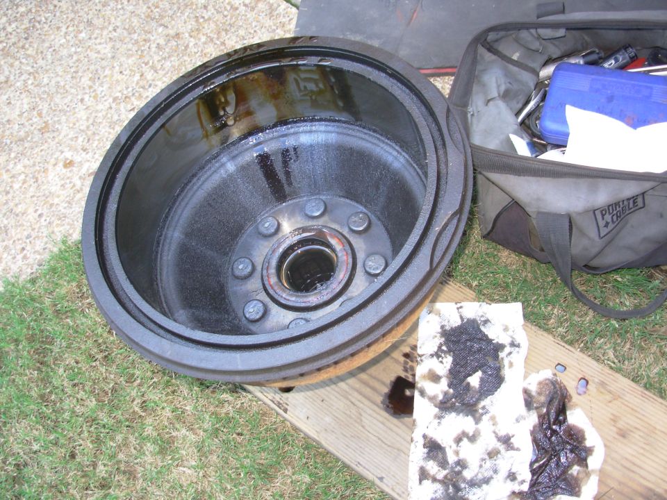 Removed brake drum and hub coated in leaked axle grease, with dirty shop towels