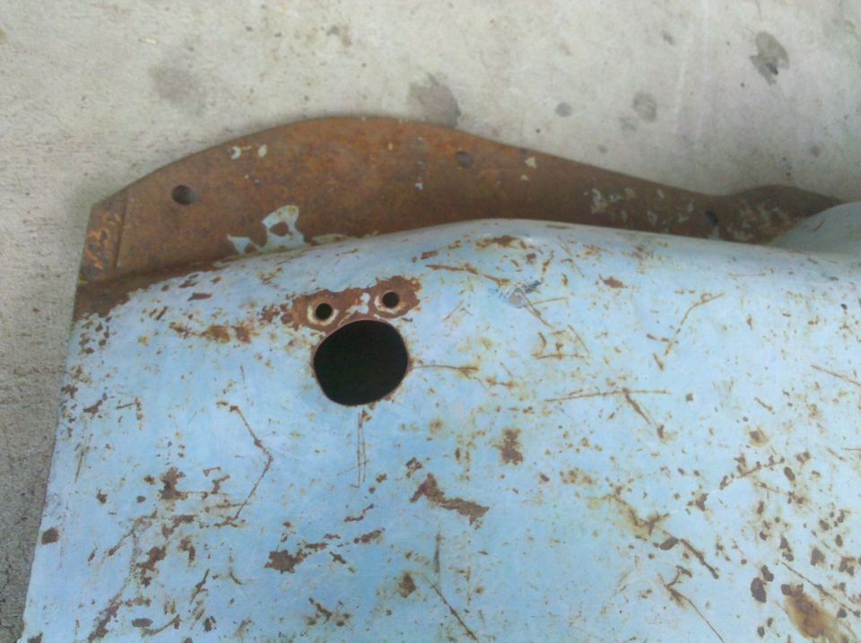 rusted light blue metal panel with a large central hole and two smaller holes above it
