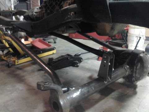 1968 Ford Bronco - Low shop-floor view of a link/coilover-style suspension conversion under a truck: a solid axle housing with welded bracketry and a triangul…