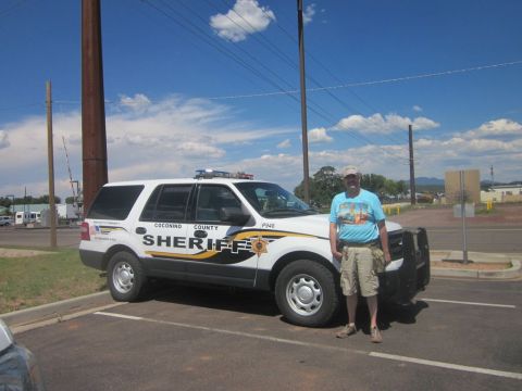 1991 Ford LTD Crown Victoria - A man stands next to a white Coconino County Sheriff's SUV, which is parked in a lot under a blue sky.