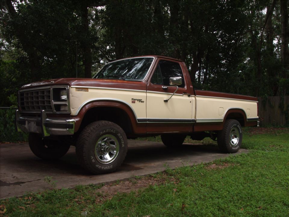Brown and tan two-tone Ford F-150 pickup truck, lifted with off-road tires, parked outdoors