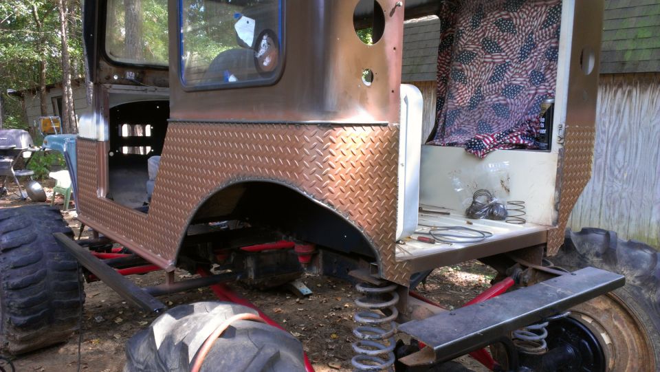 Modified off-road vehicle body with diamond plate fender flares and large tires, appears to be undergoing restoration