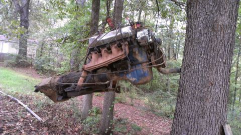 1978 Ford Bronco - Engine and transmission assembly hanging from trees in a wooded area.