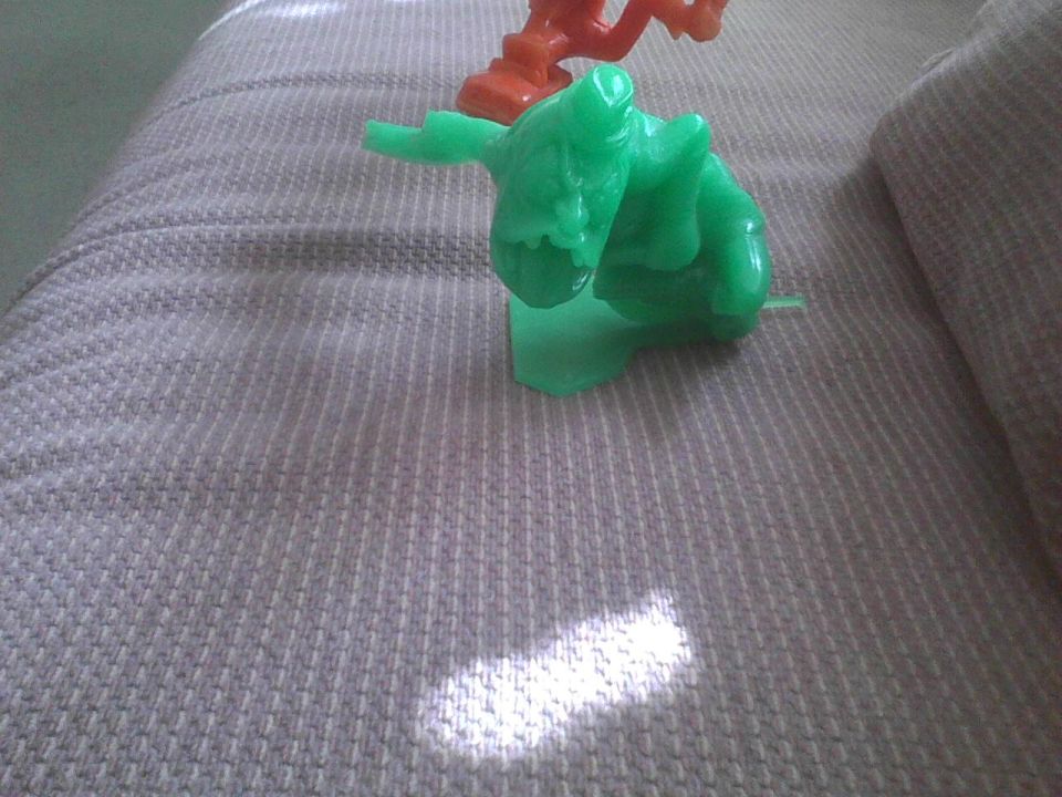 Green and orange toy figures on a textured couch with a sunbeam