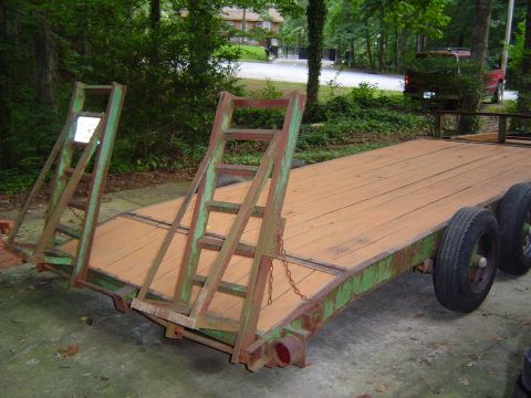 1986 Ford Bronco - A flatbed trailer with a wooden deck and green metal frame sits on a concrete surface, with trees and houses in the background.