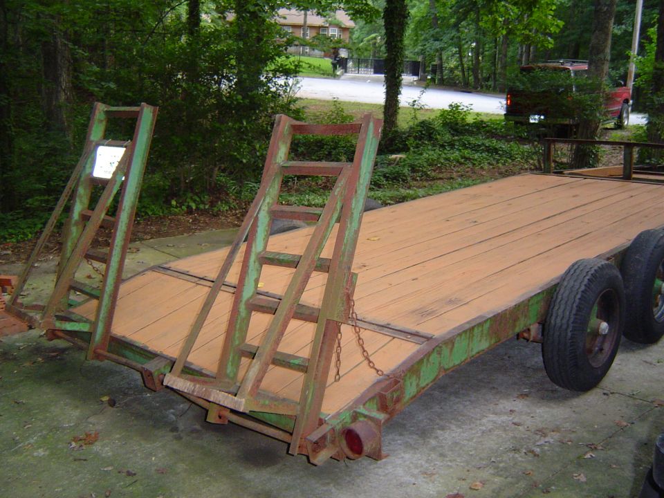 Flatbed trailer with wooden deck and green metal frame, two ramps folded up