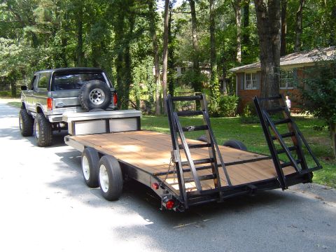 1986 Ford Bronco - A lifted 1980s Ford Bronco is hitched to a dual-axle flatbed trailer, ready for hauling.