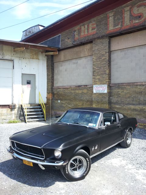 1968 Ford Mustang - A matte black 1967 Ford Mustang Fastback is parked outside a warehouse with a faded sign.