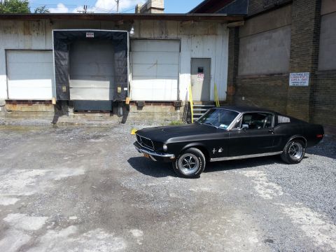 1968 Ford Mustang - A black 1967 Ford Mustang Fastback is parked outside a warehouse loading dock.