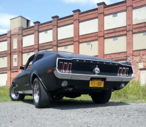 1968 Ford Mustang - Rear view of a matte black 1968 Ford Mustang parked in front of an old brick building.