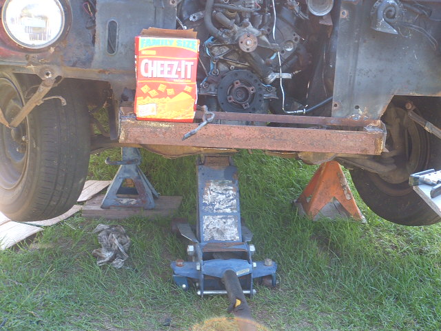 Front end of vehicle on jack stands, engine exposed, Cheez-Its box on frame