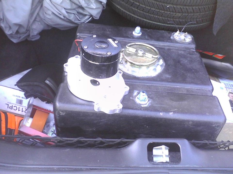 Fuel tank and pump assembly in a vehicle trunk, with a spare tire visible