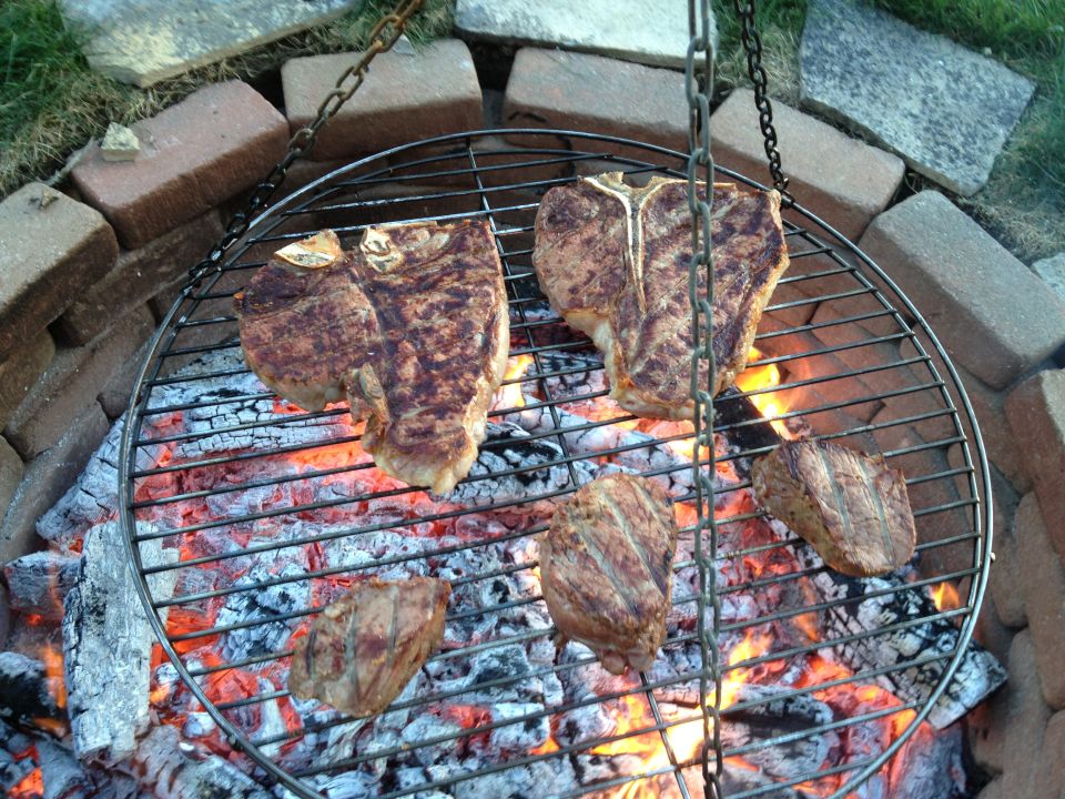 steaks cooking over coals on a round metal grill