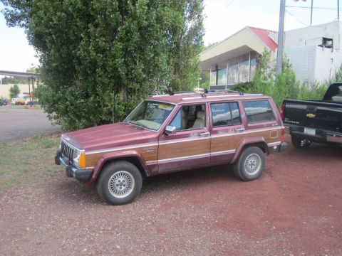 1991 Ford LTD Crown Victoria - A maroon Jeep Cherokee with wood paneling is parked next to a black Chevrolet pickup truck.