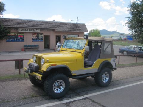1991 Ford LTD Crown Victoria - Yellow Jeep CJ with soft top parked next to a laundromat.