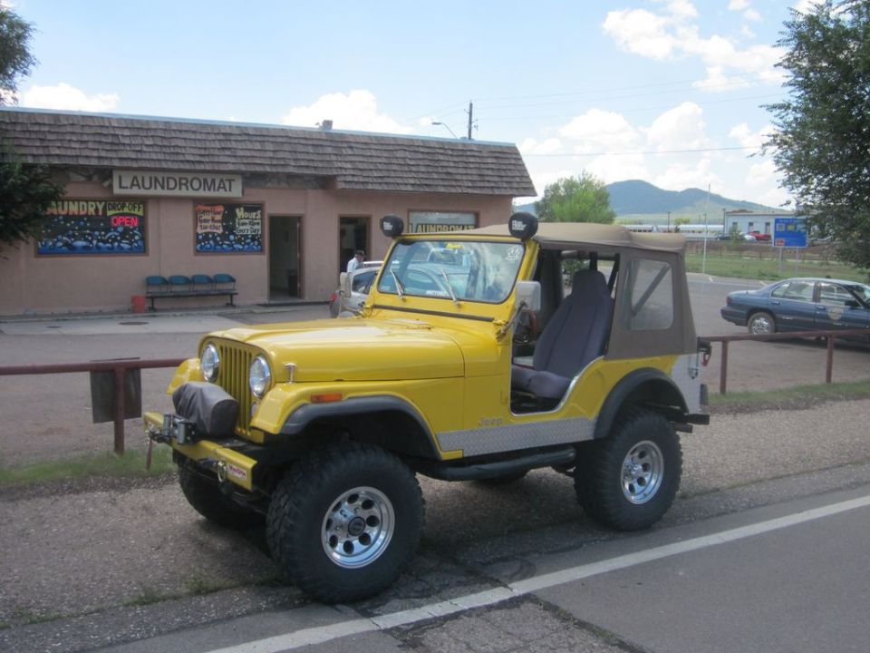 Yellow Jeep CJ parked on roadside with laundromat in background