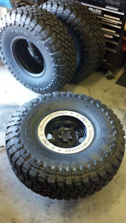 2008 Jeep Wrangler - A set of off-road tires, including one mounted on a black wheel with a silver beadlock, are displayed indoors.