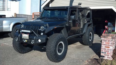 2008 Jeep Wrangler - This black Jeep Wrangler features oversized tires and a prominent front light bar, parked in a driveway.