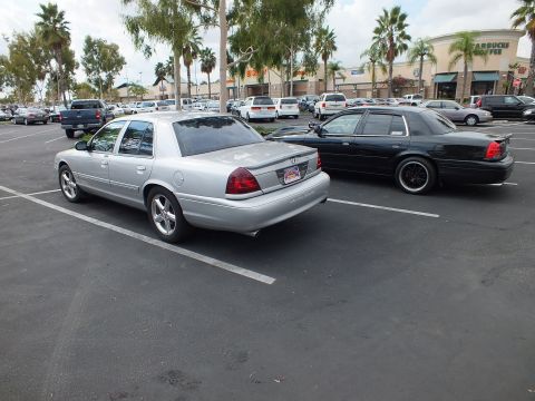 2003 Ford Crown Victoria - silver Mercury Marauder beside a black Ford Crown Victoria in a shopping center parking lot