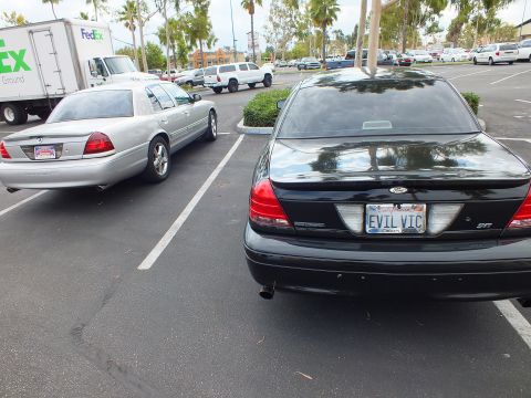 2003 Ford Crown Victoria - Black Ford Crown Victoria with EVIL VIC plate parked ahead of a silver Marauder in a lot