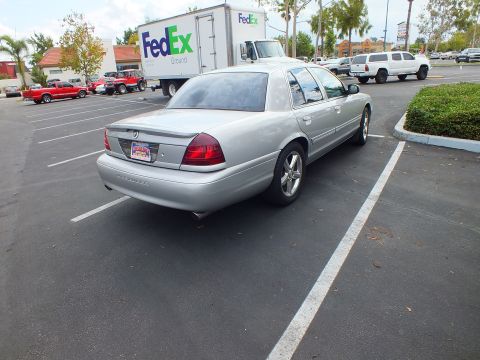 2003 Ford Crown Victoria - Silver Marauder sedan shown from the rear right quarter in a parking lot beside a FedEx truck