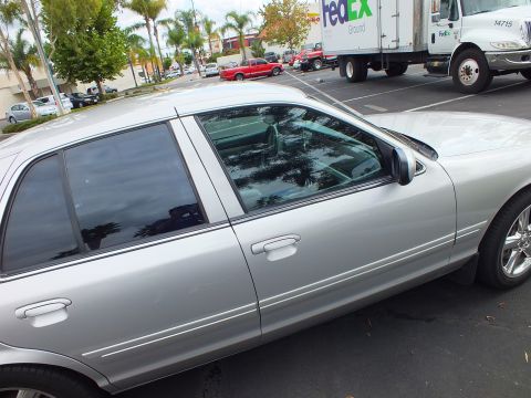 2003 Ford Crown Victoria - Tinted silver four-door sedan in a parking lot; a FedEx Ground box truck and red SUV sit in the background.