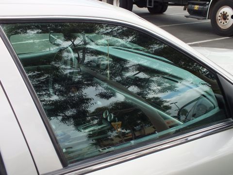 2003 Ford Crown Victoria - Detail of a sedan side window showing reflective tint; foliage and a truck wheel mirror in the glass.