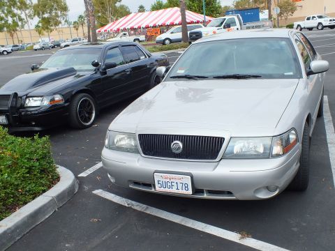 2003 Ford Crown Victoria - Close front view of a silver Mercury sedan, plate 5UGF178, with a black sedan and event tent behind.