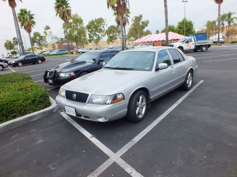 2003 Ford Crown Victoria - Silver four-door Mercury angled in a parking lot; a darker sedan and box truck sit in the background.