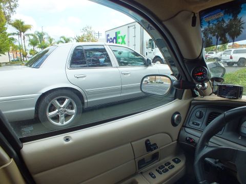 2003 Ford Crown Victoria - Cabin view through a passenger window framing a silver sedan; tan door panel and dash in foreground.