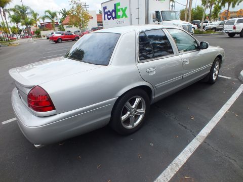 2003 Ford Crown Victoria - Rear quarter of a silver four-door sedan on polished wheels; a FedEx Ground truck sits behind it.