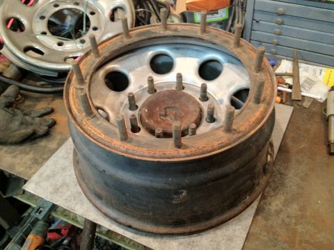 1989 Ford Bronco - A rusty truck wheel rim with visible lug studs sits on a metal surface in a workshop.